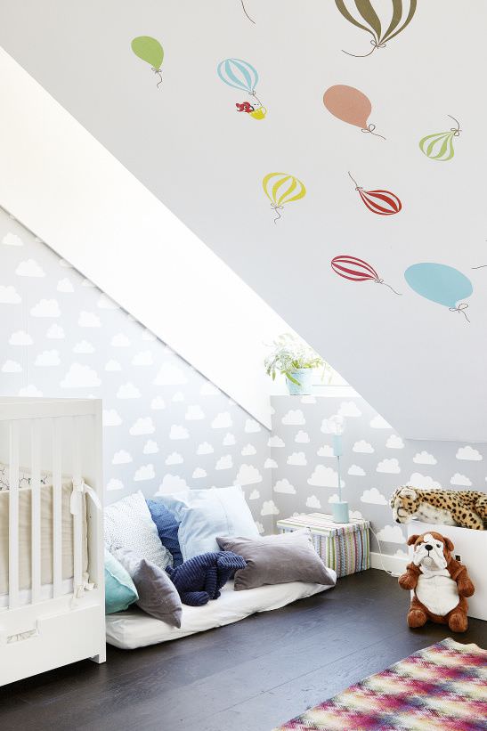 اتاق نوزاد با کاغذ دیواری خاکستری و طرح ابر که سقف آن با استیکرهای طرح بالون تزیین شده است